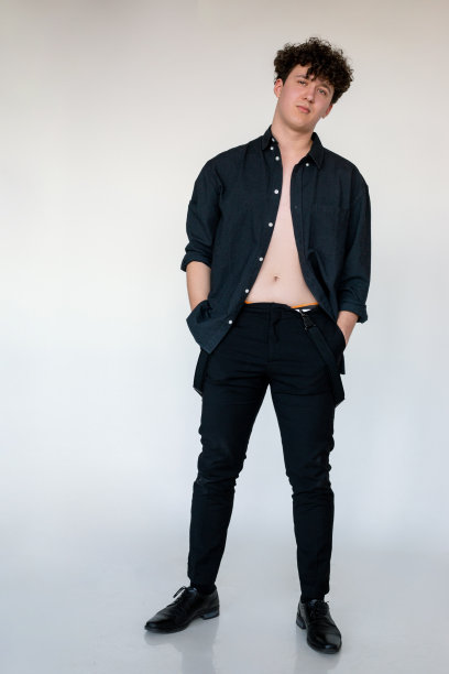 长照片的热年轻卷的家伙在黑色解开衬衫与赤裸的躯干，灰色的工作室背景。男士休闲潮装，基本款衬衫。舒适时尚的日常穿着图片下载