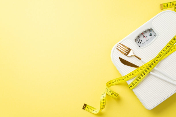 减肥的概念。俯视图照片测量胶带包裹在秤和餐具上孤立的淡黄色背景与copyspace图片下载