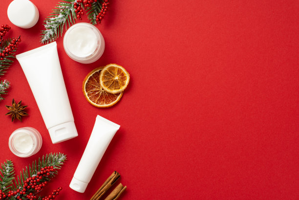 冬季护肤理念。俯视图照片白色化妆品瓶松枝在白霜槲寄生浆果干橙片肉桂棒和八角孤立的红色背景与copyspace图片下载
