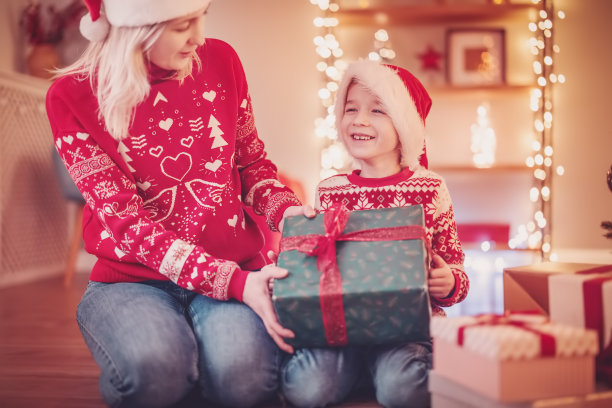 平安夜，母亲和儿子坐在室内的地板上，互送礼物盒。图片下载