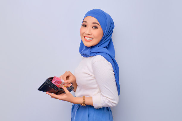 快乐的年轻美丽的亚洲穆斯林妇女展示了装满钱的钱包纸币孤立在白色背景图片下载