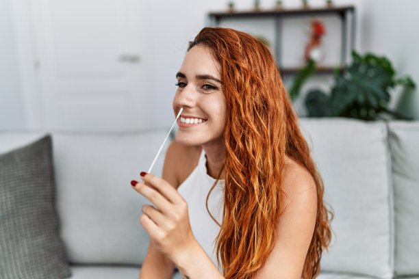年轻的红发女子微笑着自信地在家里对自己做covid-19检测图片下载