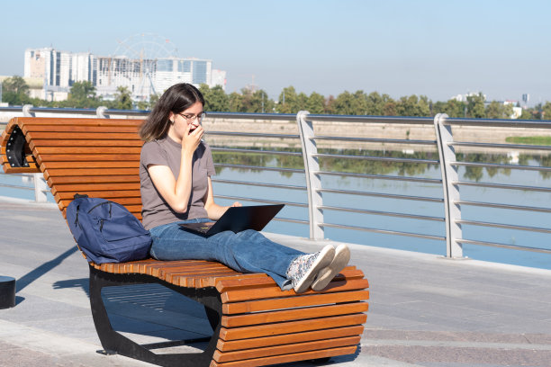一名女学生坐在城市街道的公园长凳上，用手机观看在线视频课程图片下载