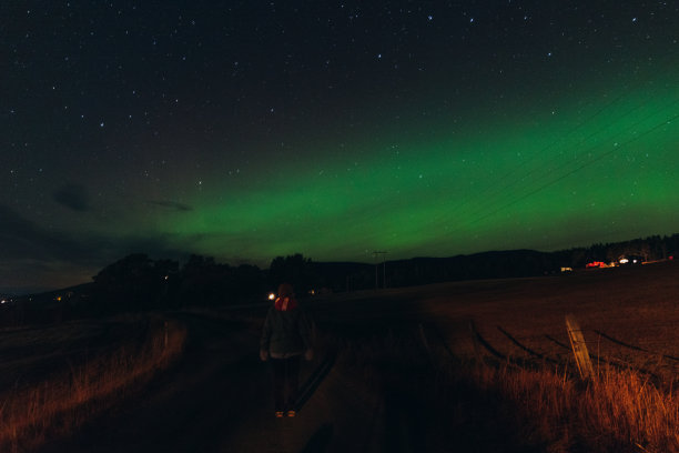 在挪威的一个村庄里，一位女士在夜晚漫步，欣赏着壮丽的北极光图片下载