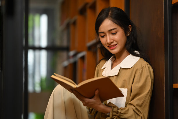 专心致志的亚洲女学生坐在书架旁看书。人、知识、教育观念。图片下载