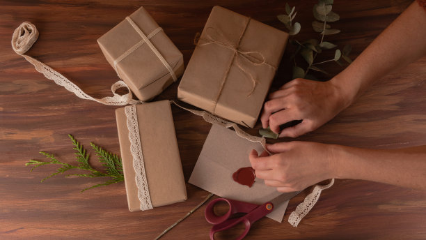 妇女双手准备礼盒与牛皮纸和黄麻丝带在木制背景图片下载