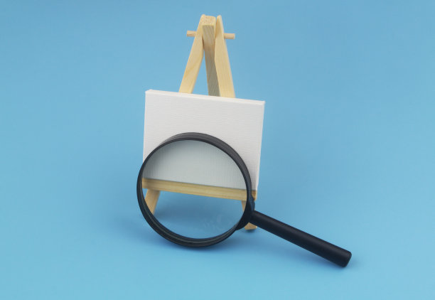 黑色放大镜和白色画布在木制画架上蓝色背景。图片下载