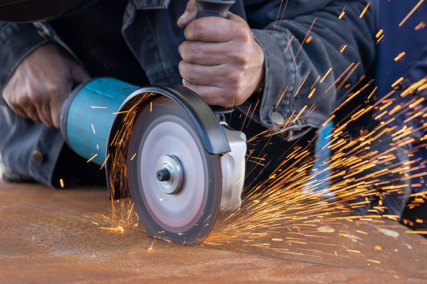 一名男工人用电磨机切割一块金属片，火花四溅。图片下载