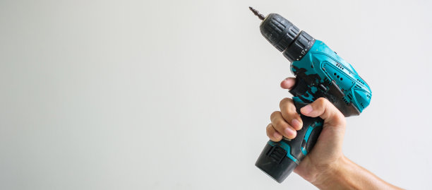 手工手持无绳螺丝刀与墙背景，木匠工作与电动螺丝刀上的工作图片下载