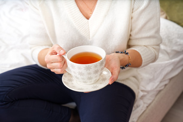 穿着白色毛衣的女孩在圣诞树的背景下端着一杯温暖的咖啡或茶。图片下载