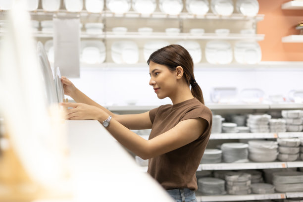 家庭主妇为她的房子买盘子、碗和一杯水。年轻女子在陶瓷商店市场大厅为食品容器挑选新项目家庭配件和家庭产品图片下载