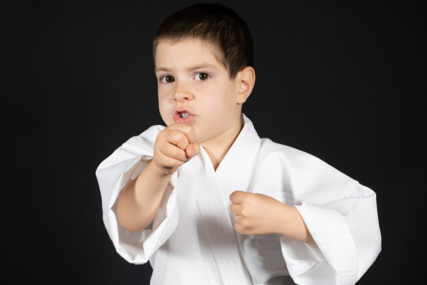 一个小男孩在练习武术，空手道课上穿着和服，黑色背景，文字的地方图片下载