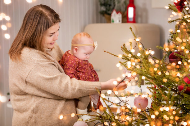 一个快乐的母亲在家里抱着婴儿玩耍，而不是在装饰好的房间和圣诞树的背景下。图片下载