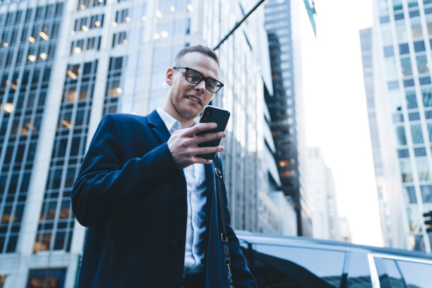 穿着外套和眼镜的自信商人在街上用手机图片下载