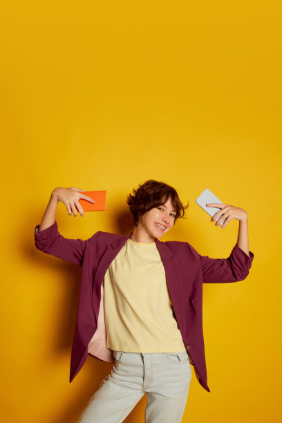 肖像的快乐少女卷曲的棕色短发摆姿势与手机孤立在黄色背景。在线交流图片下载