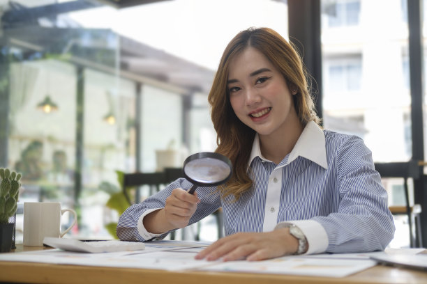 一位女商人在办公桌前用放大镜检查文件。图片下载