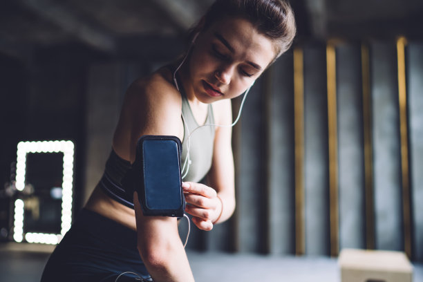近距离的图片黑发女性在耳机使用智能手机为训练检查播放列表的歌曲，运动员准备训练搜索手机播放器和歌曲使用声音配件图片下载