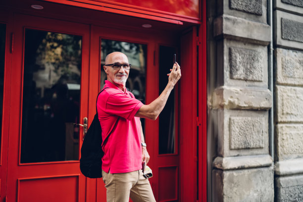 老年男性60岁，在退休度假时用手机拍摄旅行视频日志，半长白人男子用现代智能手机拍摄城市街道图片下载