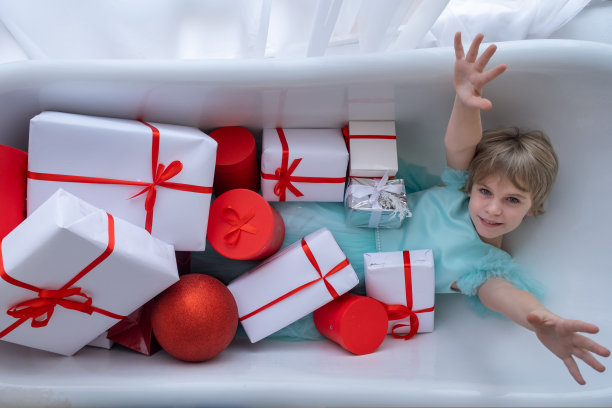 少女在装满礼品盒的浴缸里泡澡，圣诞节概念图片下载