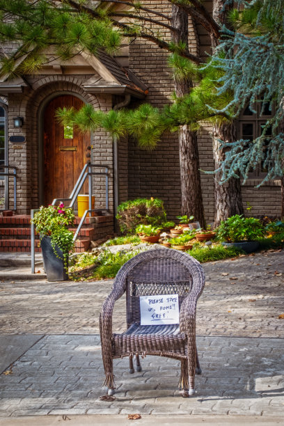 破旧的柳条椅子放在屋前的路缘上，上面写着“请送我回家”的牌子图片下载