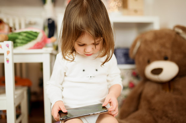 小女孩在用智能手机。卧室里有手机的孩子的特写画像。可爱的小女婴肖像在家里，童年，家庭概念。图片下载