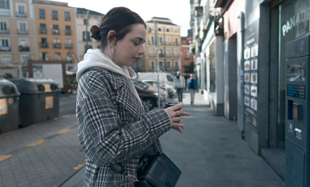 年轻女子在街上端着一杯热气腾腾的咖啡。图片下载