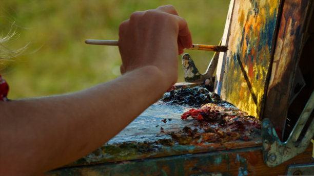 画家手在画架上绘画特写。艺术家在调色板上混合颜料。图片下载