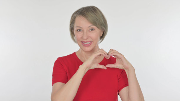 老妇人用手在黄色背景上展示心形图片下载