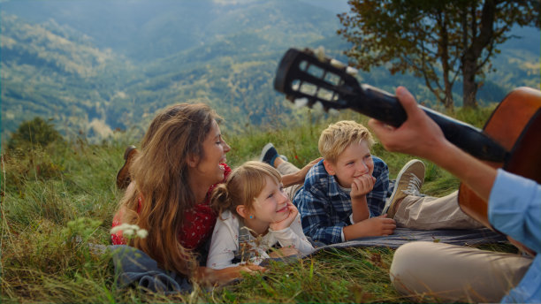 男子弹吉他野餐为妻子和孩子近距离。幸福的家庭听着音乐。图片下载