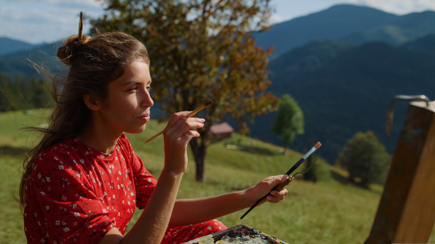 女艺术家在调色板上混合颜料，画出绿色的草地特写。图片下载