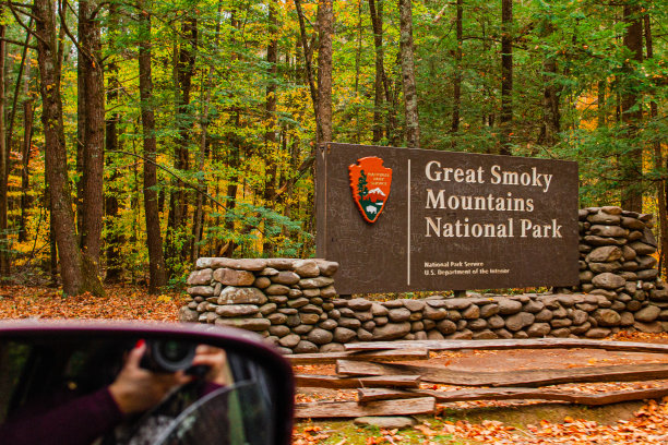 2022年秋天，一名女子在田纳西州大烟山国家公园的入口招牌上拍照，背景是五颜六色的秋树图片下载