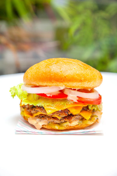 绿色背景的咖啡厅，白色桌子上放着双层起司美式汉堡。图片下载