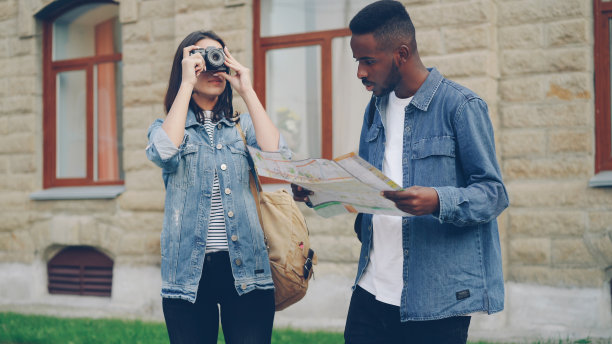 英俊的非洲裔美国男子正在看地图，而他迷人的女性朋友正站在市中心用相机拍照聊天。图片下载