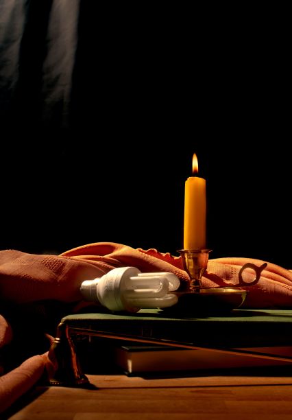 垂直静物画，16世纪风格的书上有燃烧的蜡烛和现代灯泡。图片下载