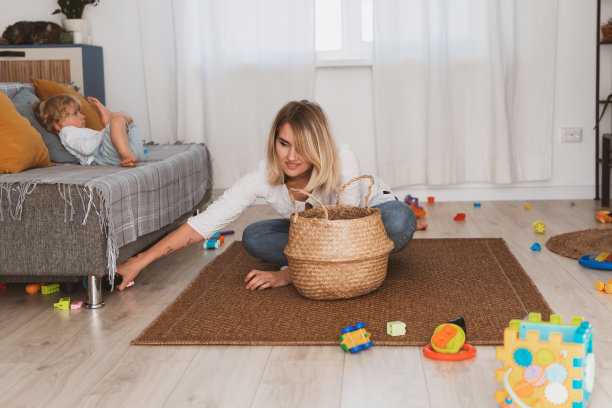 年轻的妇女，家庭主妇把玩具放在篮子里，她的小儿子在家里图片下载