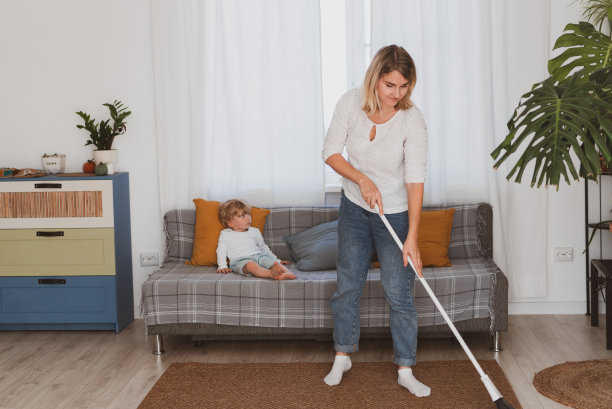 年轻的妇女，家庭主妇和她的小儿子一起在家里用扫帚打扫图片下载