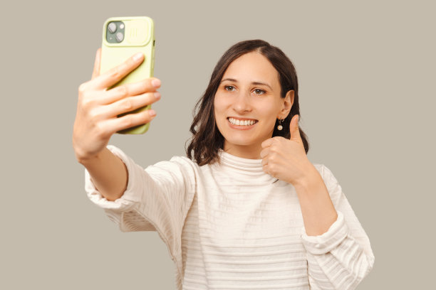一名微笑的女子竖起大拇指，用手机自拍。图片下载