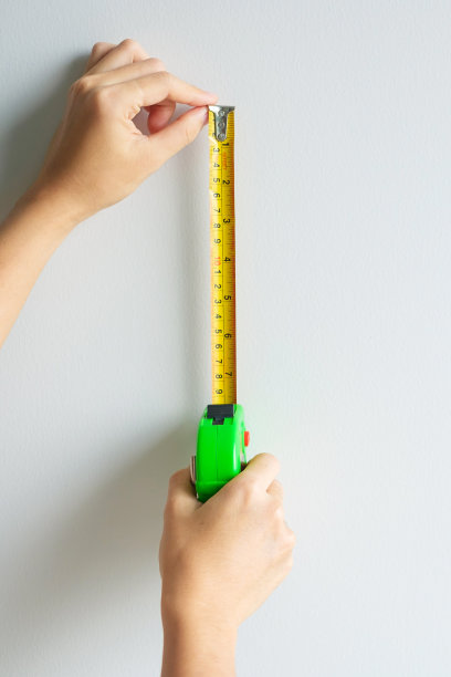 在家里用卷尺测量墙面背景。DIY，室内设计，维修和改善家庭或公寓概念图片下载