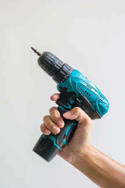 手工手持无绳螺丝刀与墙背景，木匠工作与电动螺丝刀上的工作图片下载