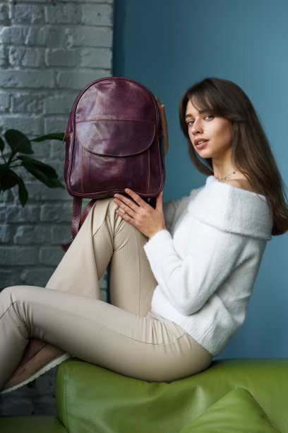美丽苗条的女孩在米色裤子和橄榄色毛衣摆姿势与紫色的小皮革背包图片下载