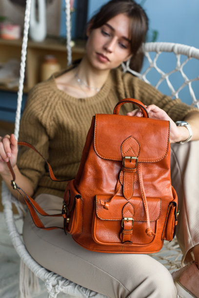 美丽苗条的女孩，米色裤子和橄榄色毛衣摆姿势，坐在秋千椅上，带着一个闪闪发光的橙色小皮革背包图片下载