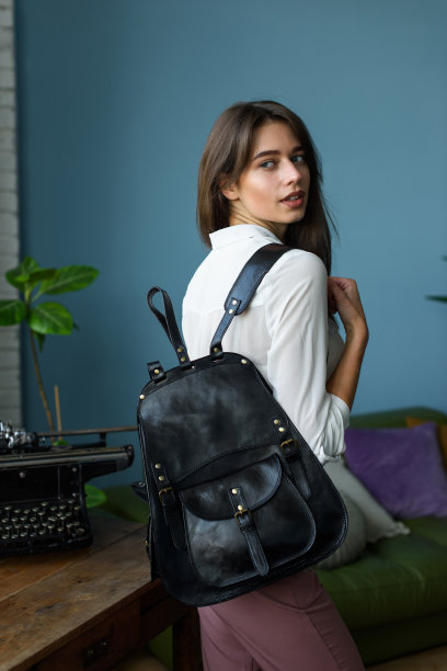 美丽苗条的女孩在酒红色的裤子和一件白色衬衫摆着一个黑色的皮革背包图片下载