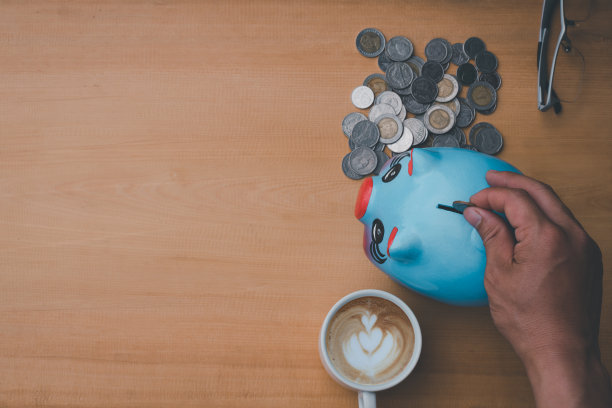 俯视照片的猪，硬币和咖啡杯，一只手把硬币放在储蓄罐上的木制背景图片下载