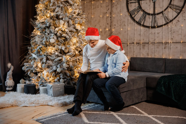 爸爸和儿子孩子们坐在圣诞树旁边看书图片下载