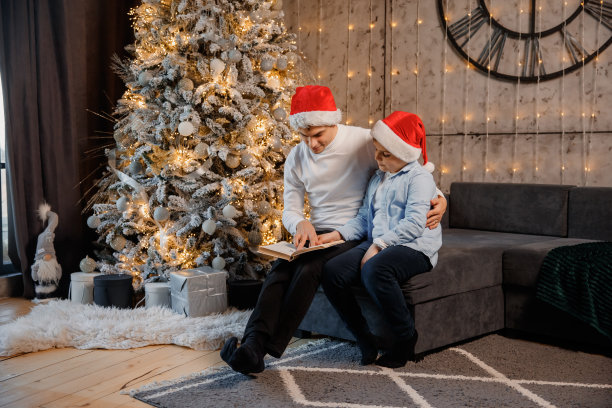 爸爸和儿子孩子们坐在圣诞树旁边看书图片下载