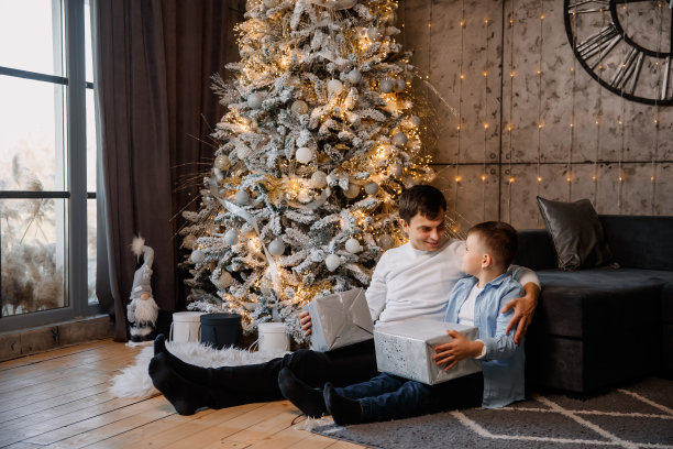 爸爸和儿子孩子坐在圣诞树旁边，举行圣诞节图片下载