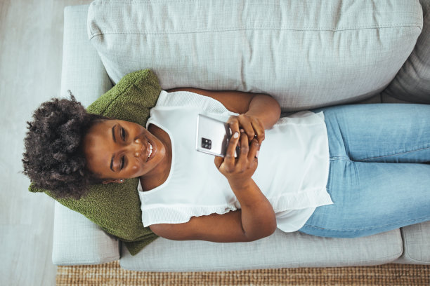 一个迷人的年轻女子使用她的手机，而坐在客厅在白天的短镜头图片下载