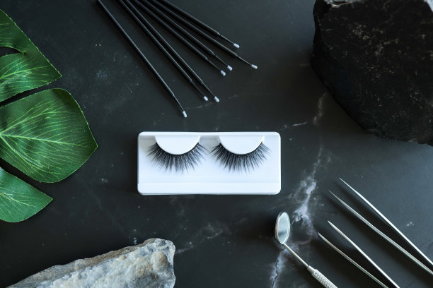 睫毛延伸工具在时髦的黑色背景和石头。假睫毛，镊子和刷子。美容沙龙。妆化妆品。俯视图，平铺图片下载