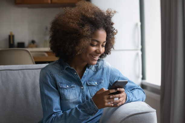 非洲少女坐在沙发上用智能手机图片下载