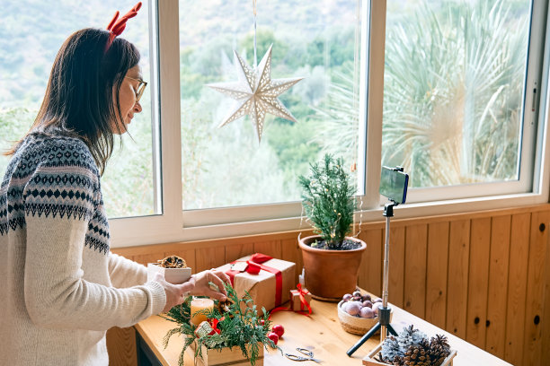 女花匠博主在她的智能手机前用新鲜的松枝、蜡烛和圣诞装饰制作冬季花道。小生意。季节性冬季车间。图片下载